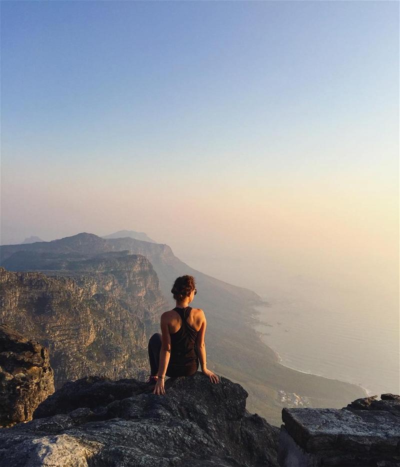A woman sitting on top of a mountain overlooking the ocean.
