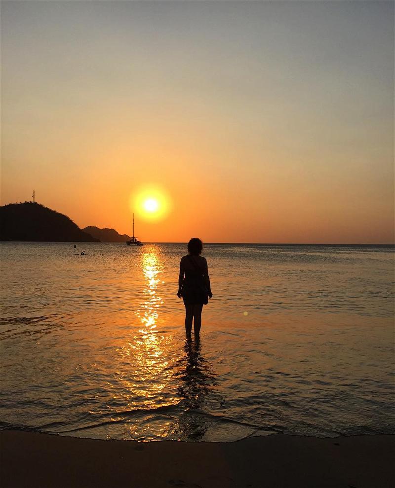 A woman standing in the water at sunset.