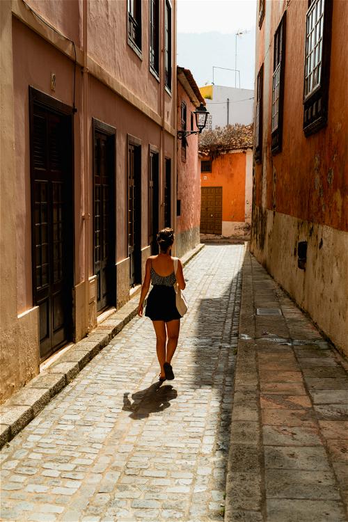 Woman walking down a historic narrow street between pink and orange painted walls in the Canary Islands