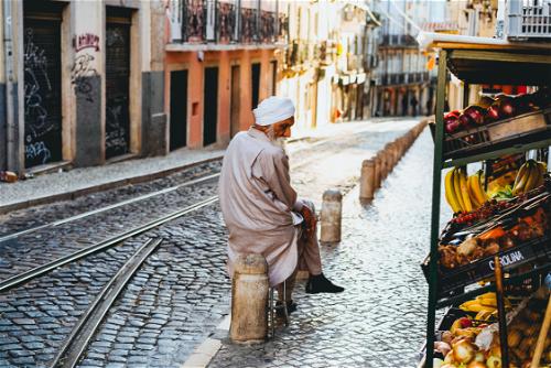 Man in a beige robe wearing a white turban sitting on a cobblestone street in Lisbon Portugal