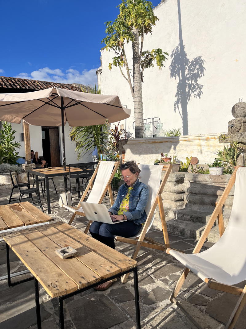 A person using a laptop on a wooden deck chair.