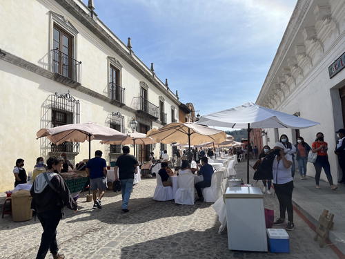 People walking down a cobblestone street with tables and umbrellas.