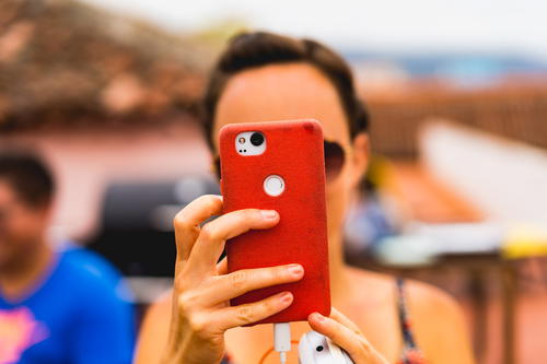 A woman is taking a picture of her phone with a red case.