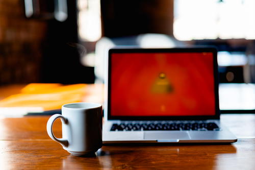 Big white coffee mug next to a MacBook Pro on a wooden table desk in a coworking space