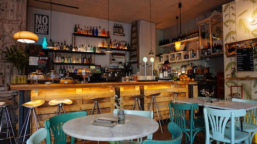 Interior of a cozy cafe, with white quartz tables and blue and teal wooden chairs next to a wooden bar