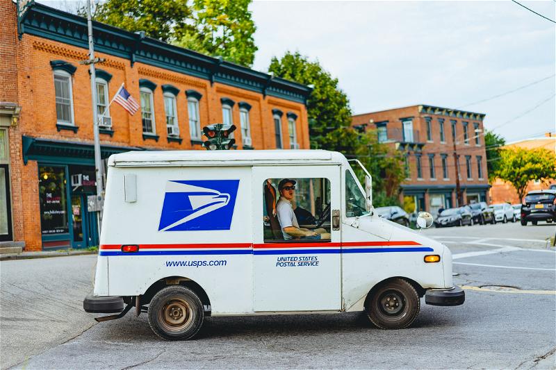 A man driving a mail truck on a street.