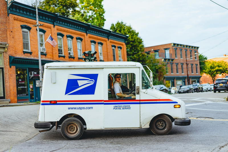 A man driving a mail truck on a street.