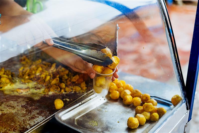 A hand using tongs to put tiny fried potatoes into a plastic cup at a street food vendor stall in Guatape.