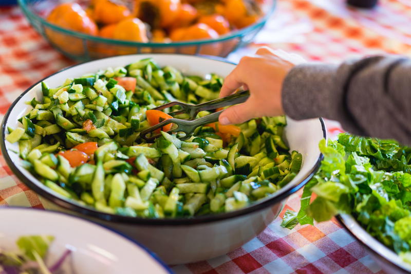 A woman uses a salad tong to take Israeli salad from a big white bowl on a breakfast table at Abraham Hostel, Jerusalem.