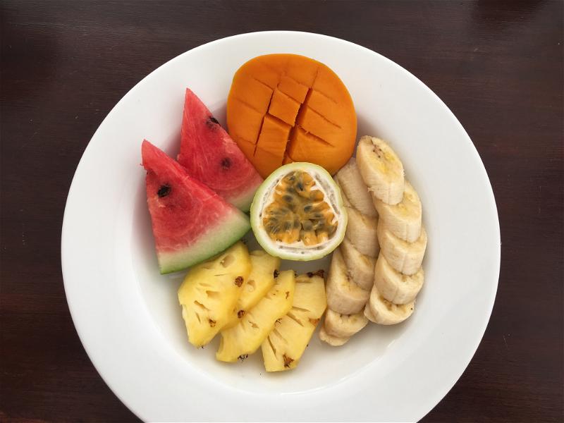 Sri Lankan fruits of watermelon, mango, passionfruit, pineapple and banana on a white plate on a wood table.