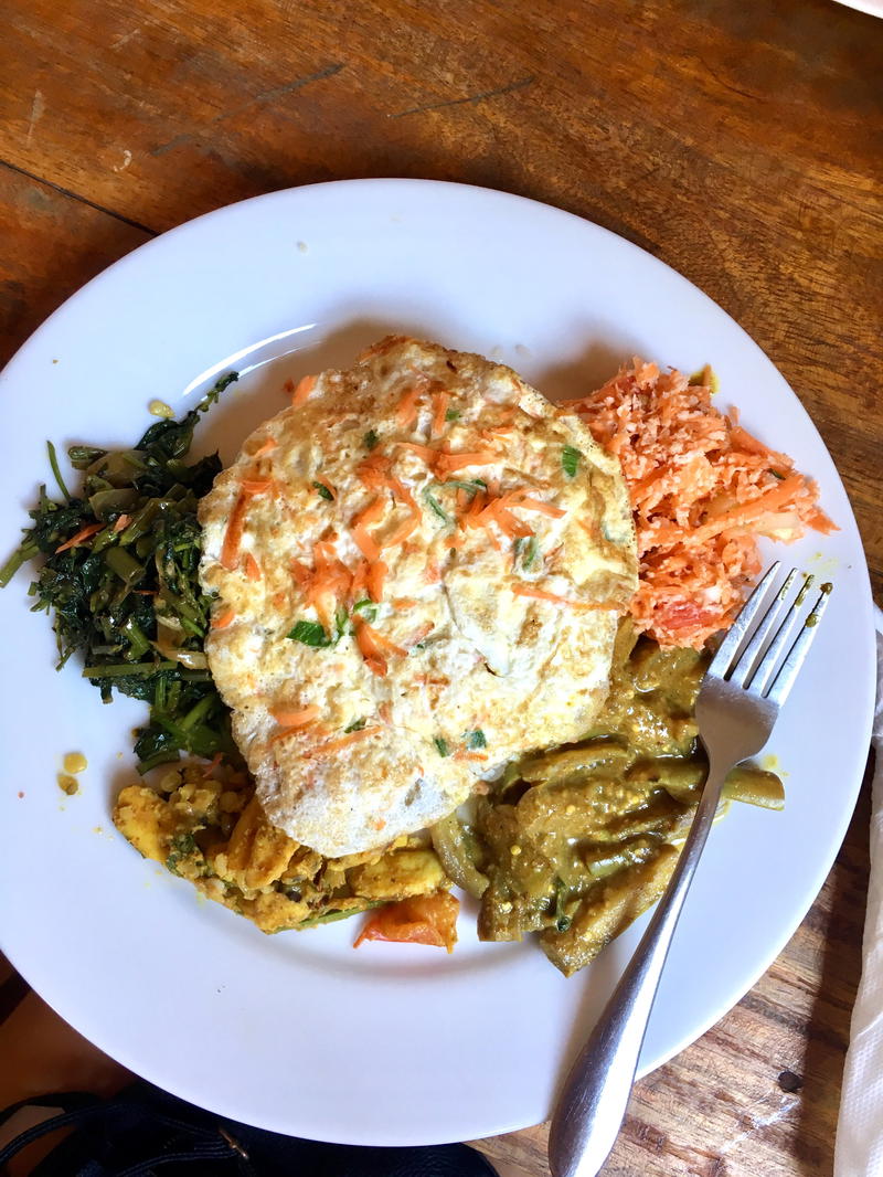 Typical Sri Lankan vegetarian lunch with fried egg, coconut sambal, fried vegetables and a metal fork on a white plate in Mirissa, Sri Lanka.