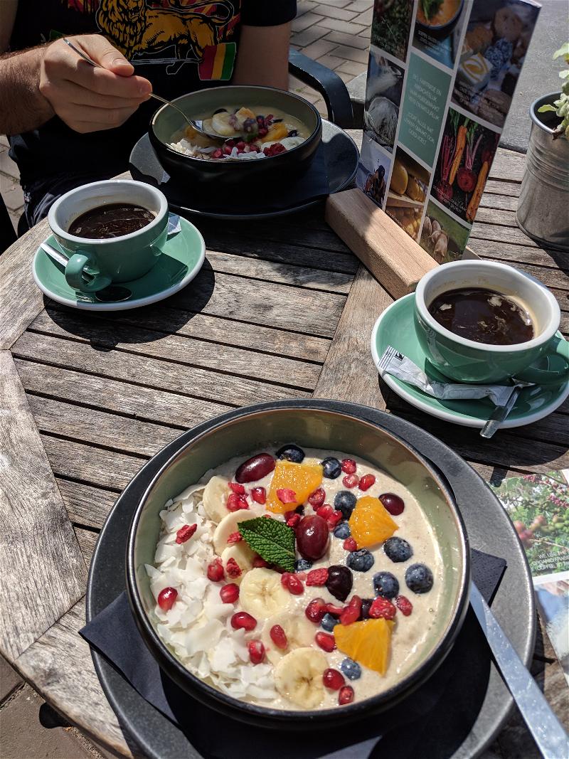 Fruit and oatmeal bowl at an outdoor cafe with two coffee cups in the Eastern Docks, Amsterdam, Netherlands.