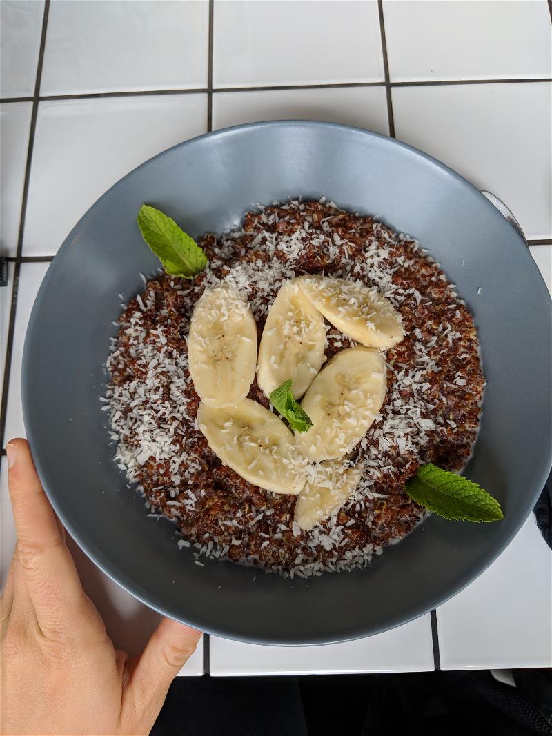 Chocolate oatmeal bowl with sliced banana and mint on top on a white tiled table at a cafe in Tallinn, Estonia.