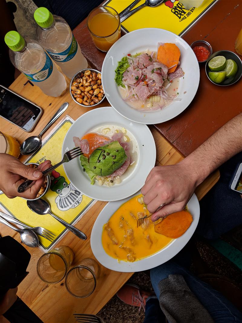 Top-down view of three plates on a wooden table containing different types of Peruvian ceviche for lunch at a restaurant in Lima.