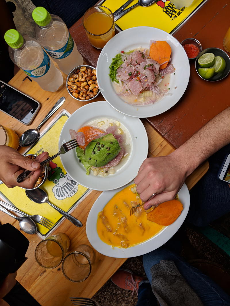 Top-down view of three plates on a wooden table containing different types of Peruvian ceviche for lunch at a restaurant in Lima.