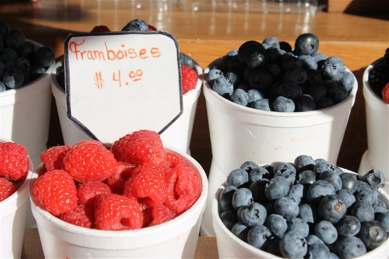 Raspberries and blueberries in white styrofoam cups at a farmer's market.