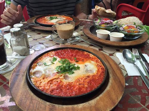 Shakshuka on a wooden plate on a tiled table at the shuk in Jerusalem, Israel.