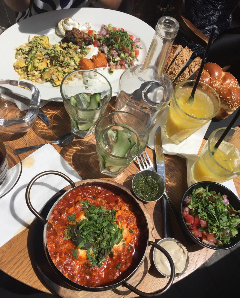 Brunch at a restaurant, with eggs and hot shakshuka on a wooden table in Downtown Tel Aviv, Israel.