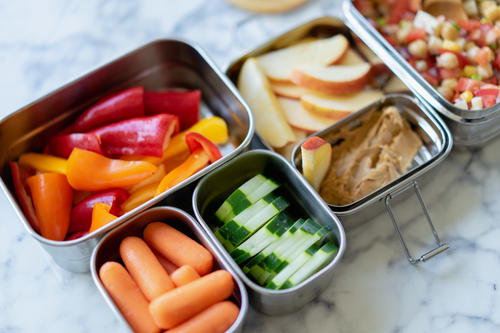 A lunch box filled with carrots, cucumbers, and hummus.