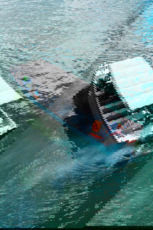 Motorized boat with a roof cover and smoke coming out the back in a river