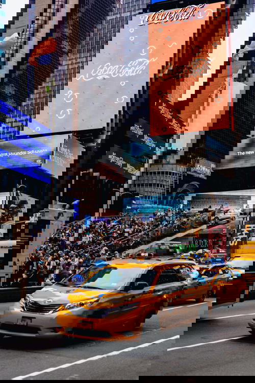 Times Square scene with a big Coca Cola billboard and yellow NYC minivan taxi