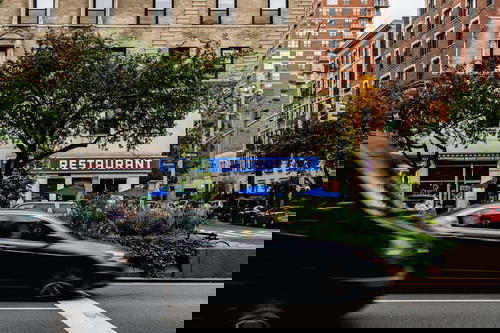 Cars driving by Broadway on the upper west side near the seinfeld restaurant