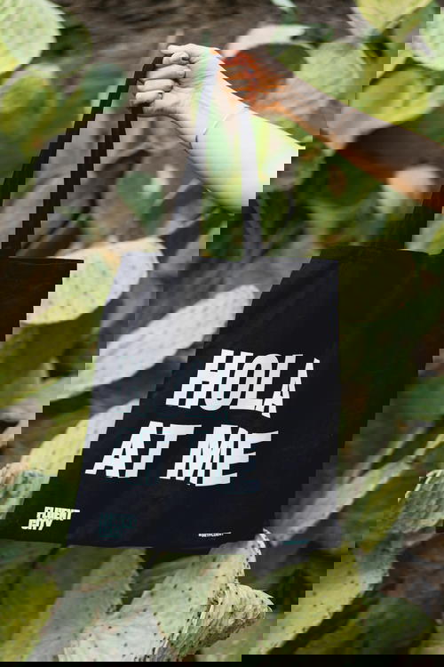 Black canvas tote bag with HOLA AT ME text in front of cacti
