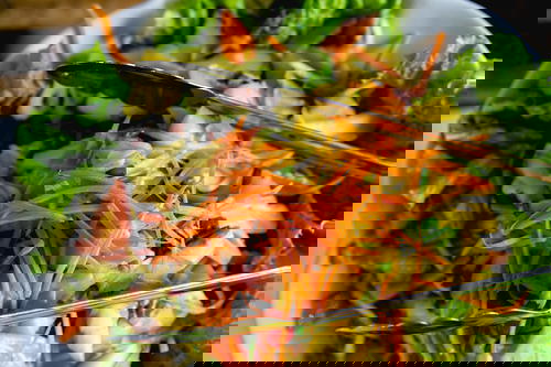 A bed of green lettuce, chopped pineapple and shredded carrots in a white bowl with silver tons