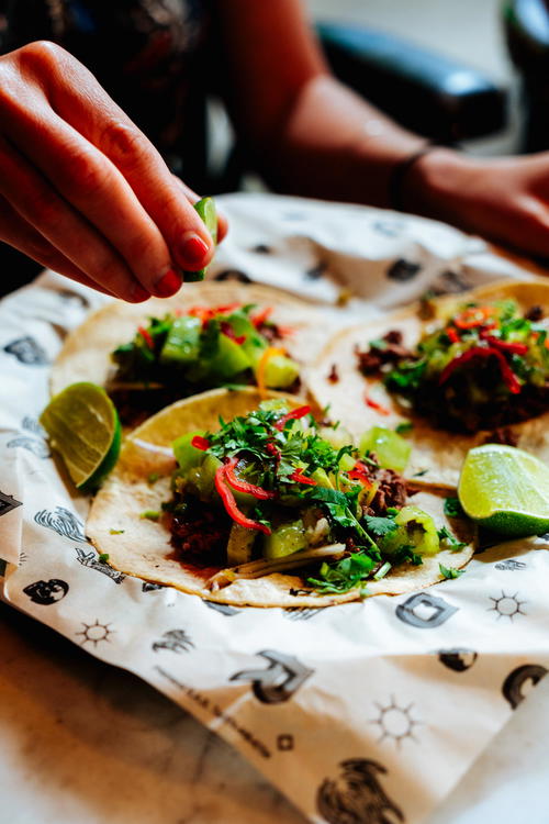 Woman squeezing a lime slice onto a taco in a set meal of three meat tacos