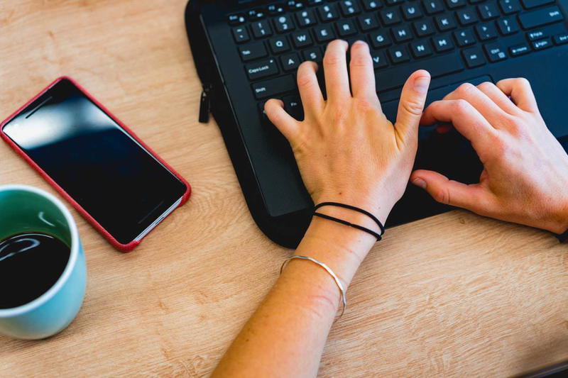 A woman typing on a laptop with a cup of coffee.