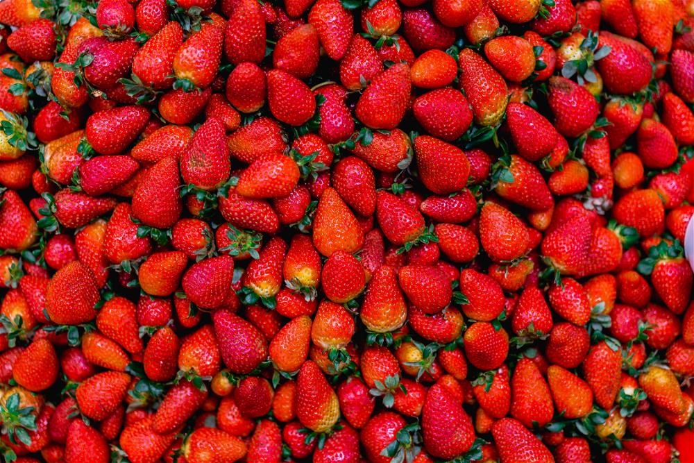 Piles of red strawberries with green leafy tops in a market