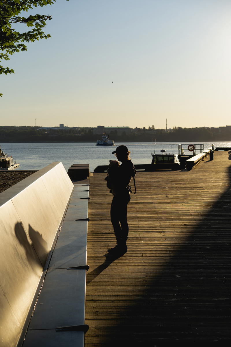 A women with a baby in a carrier with harsh AM morning light on the boardwalk in Halifax.
