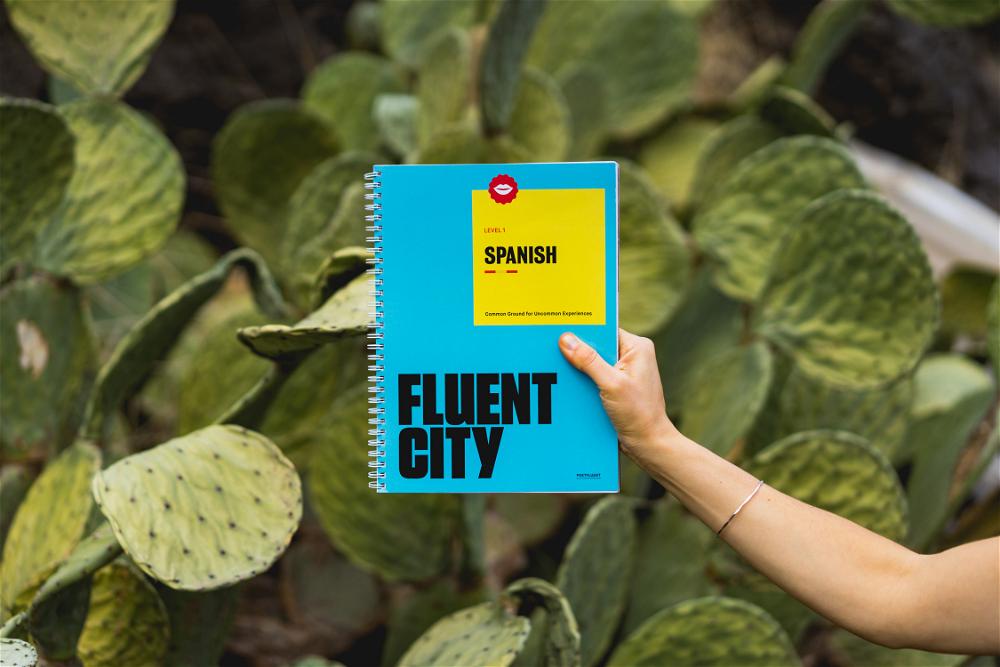 A person holding a notebook with the words fluent city in front of a cactus.