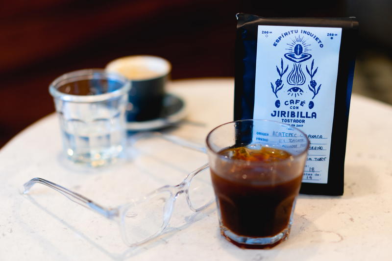 A glass of coffee and a bag of coffee sit on a table.