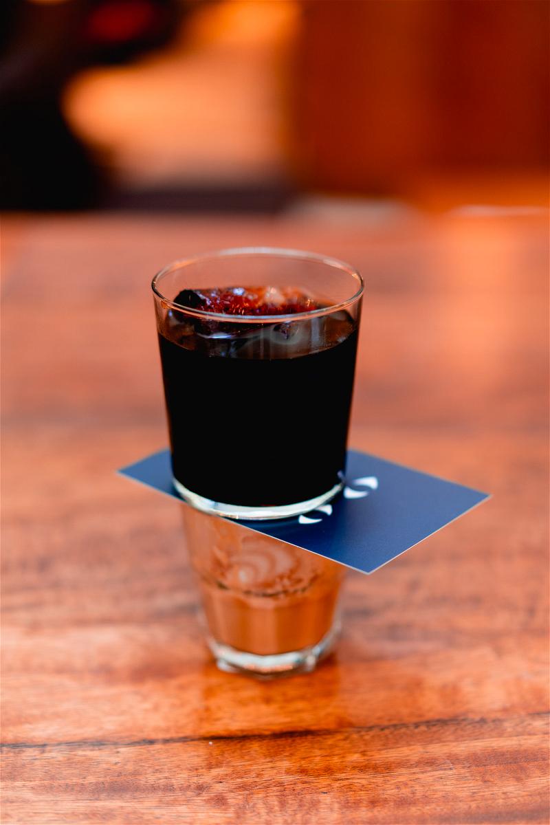 A black drink in a glass on a wooden table.