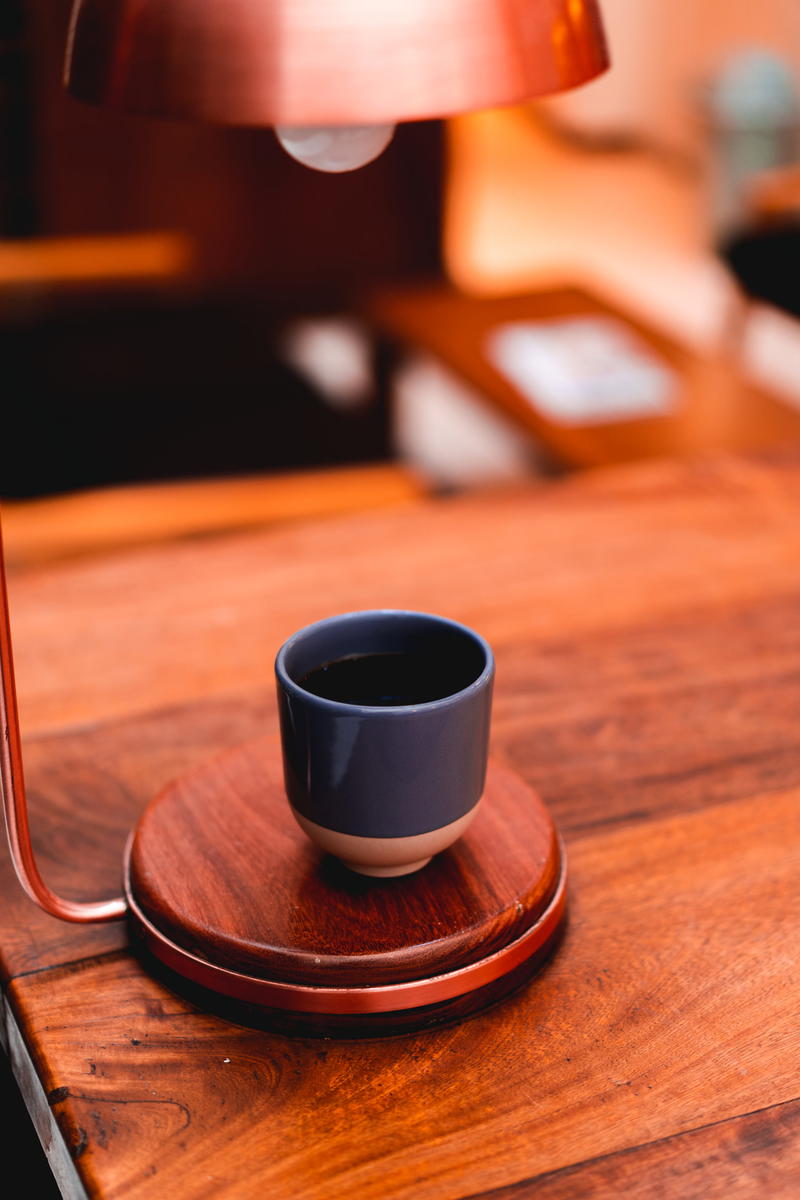 A cup of coffee on a table next to a lamp.