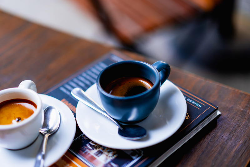 Two cups of coffee on a table next to a book.