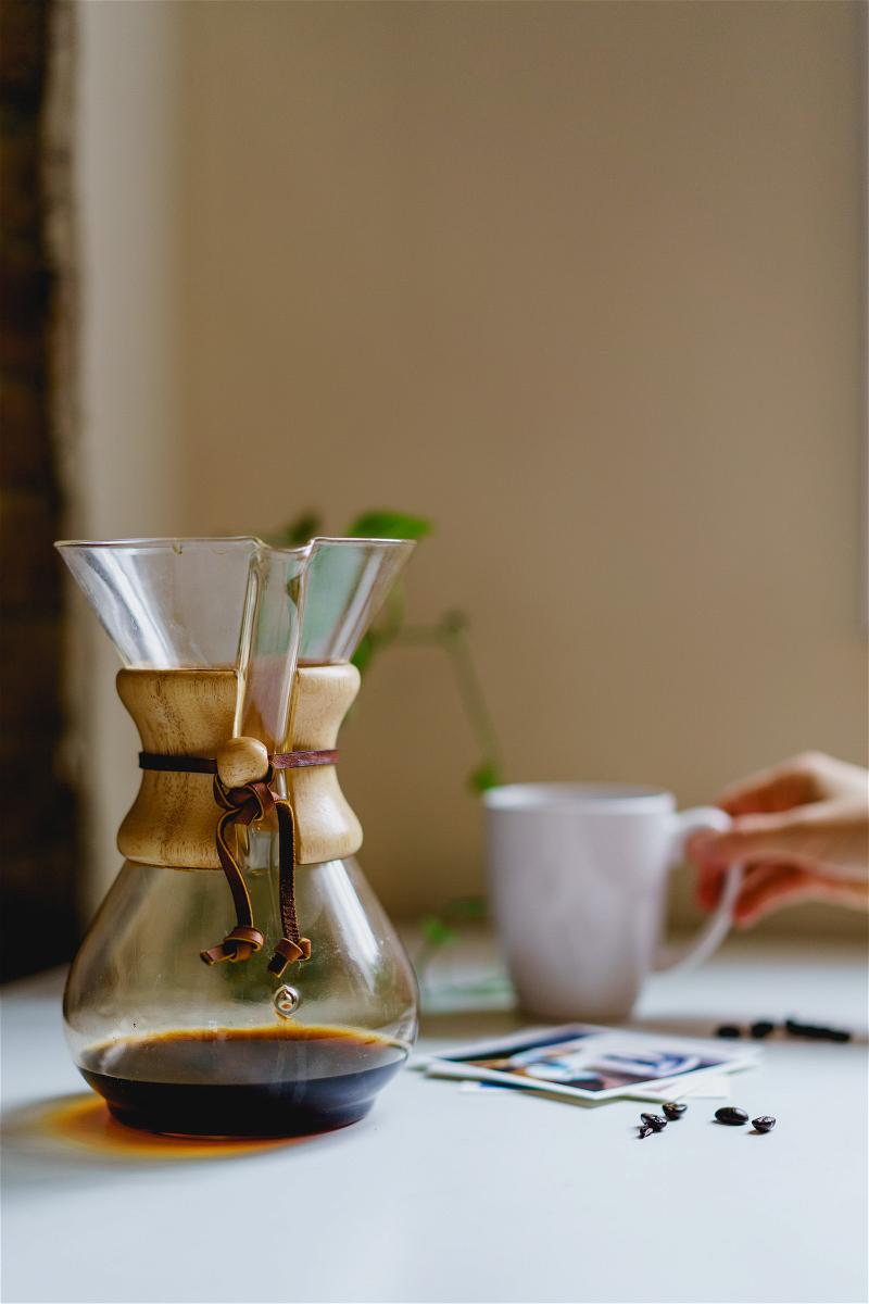 A Chemex on a table next to a cup of coffee.