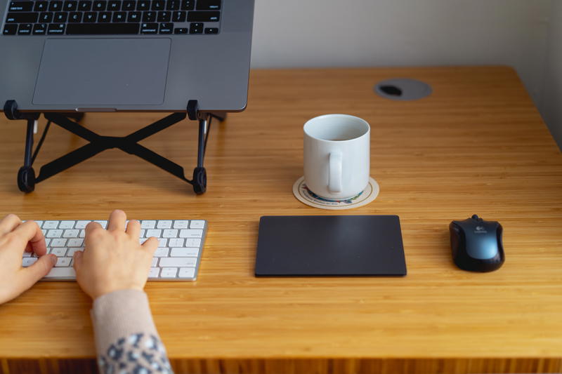 A woman typing on a laptop on a wooden desk.