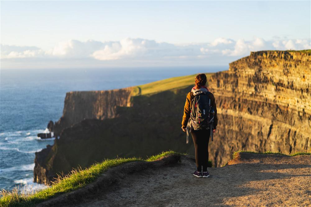 Woman wearing a backpack looking into the distance at the Cliffs of Moher Ireland