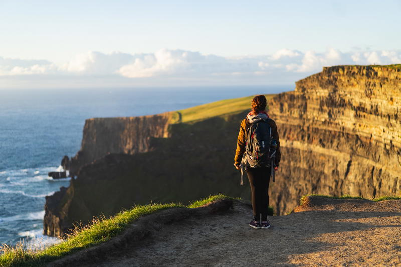 Woman wearing a backpack looking into the distance at the Cliffs of Moher Ireland