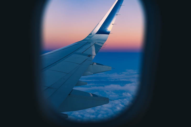 Wing of an airplane against a pink and purple sunset framed by an airplane window