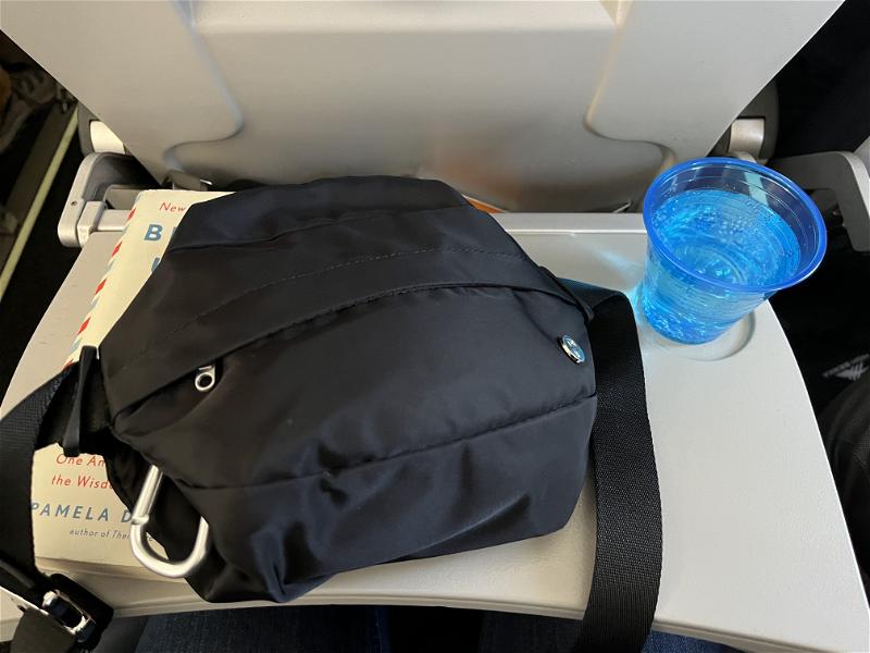 An airplane seat with a Public Rec Adapt Belt Bag and a cup of water.