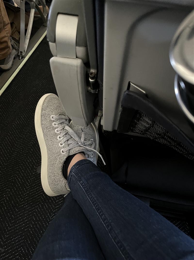 A person's feet on the seat of an airplane.