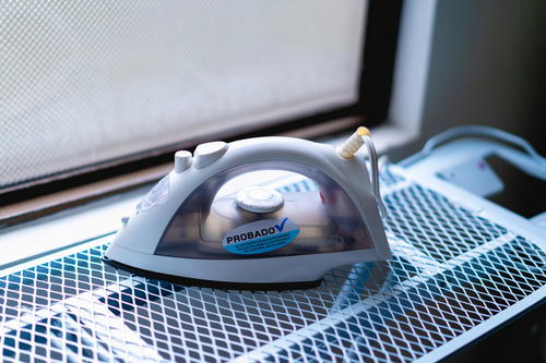 Iron with a tag in Spanish on a white metal ironing board