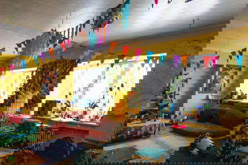 Banner flags and multi-colored furniture in a hostel common area with yellow walls and guitars hanging on the walls