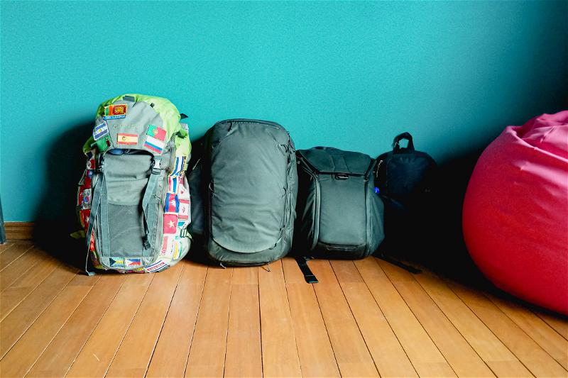 Row of backpacks taken on a trip by a couple, against a teal wall and with a red beanbag chair