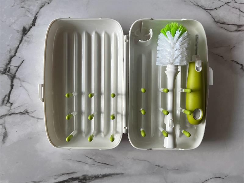 A white container with a green toothbrush and a green brush.
