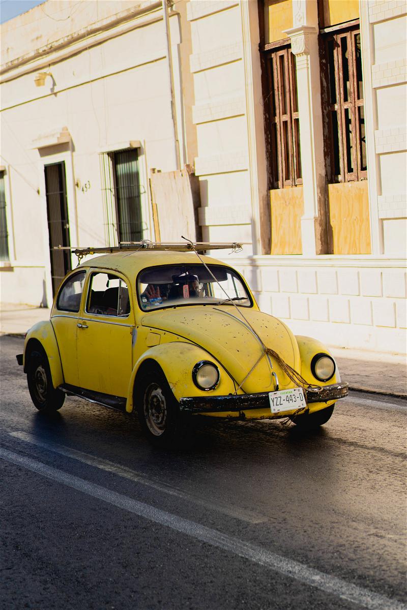 A yellow volkswagen beetle driving down the street.