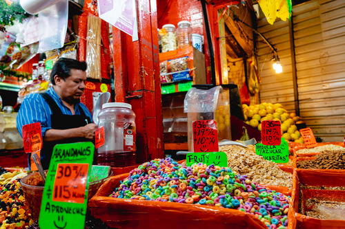 Old man in blue striped shirt with a black apron filling candy at a market